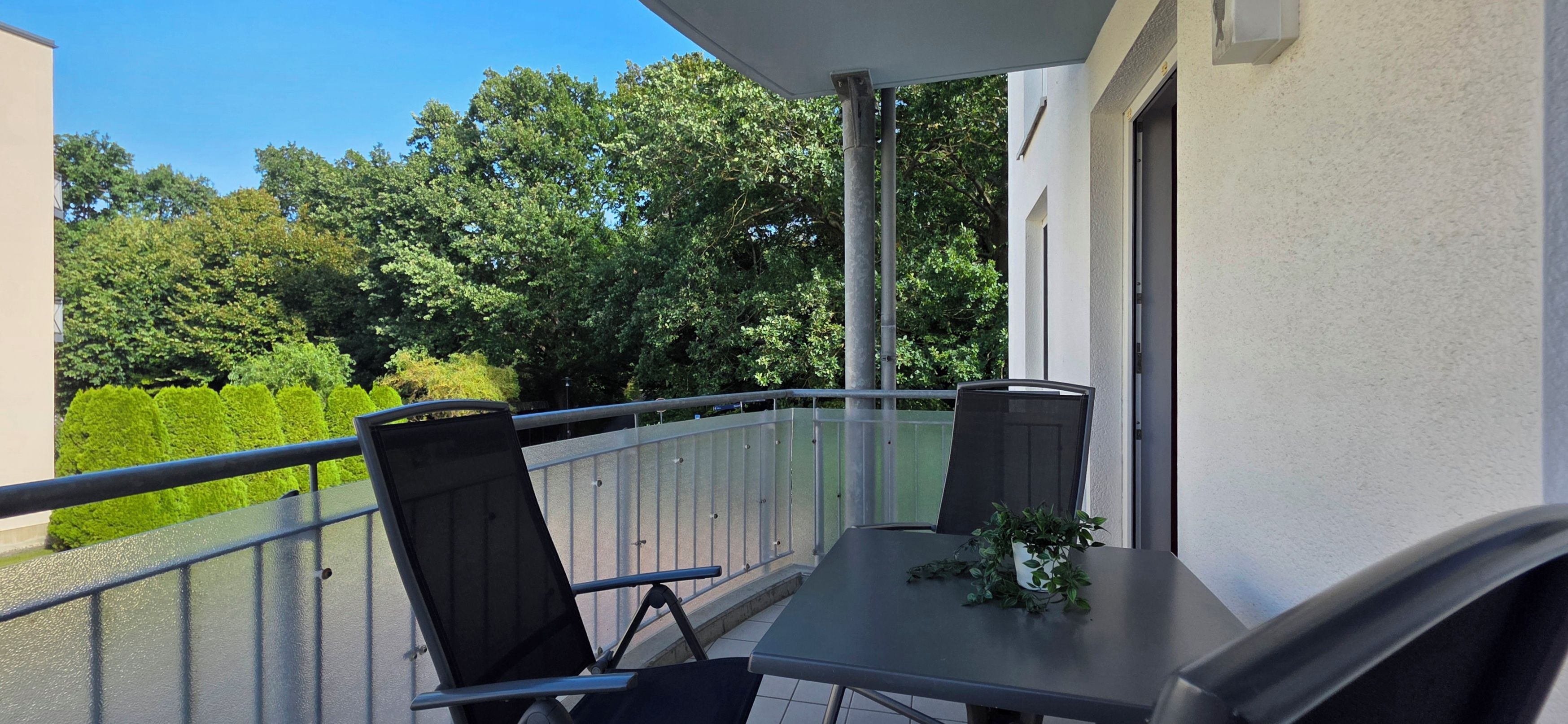 Ein Balkon mit zwei Stühlen und einem Tisch, mit Blick auf einen Garten und Bäume.