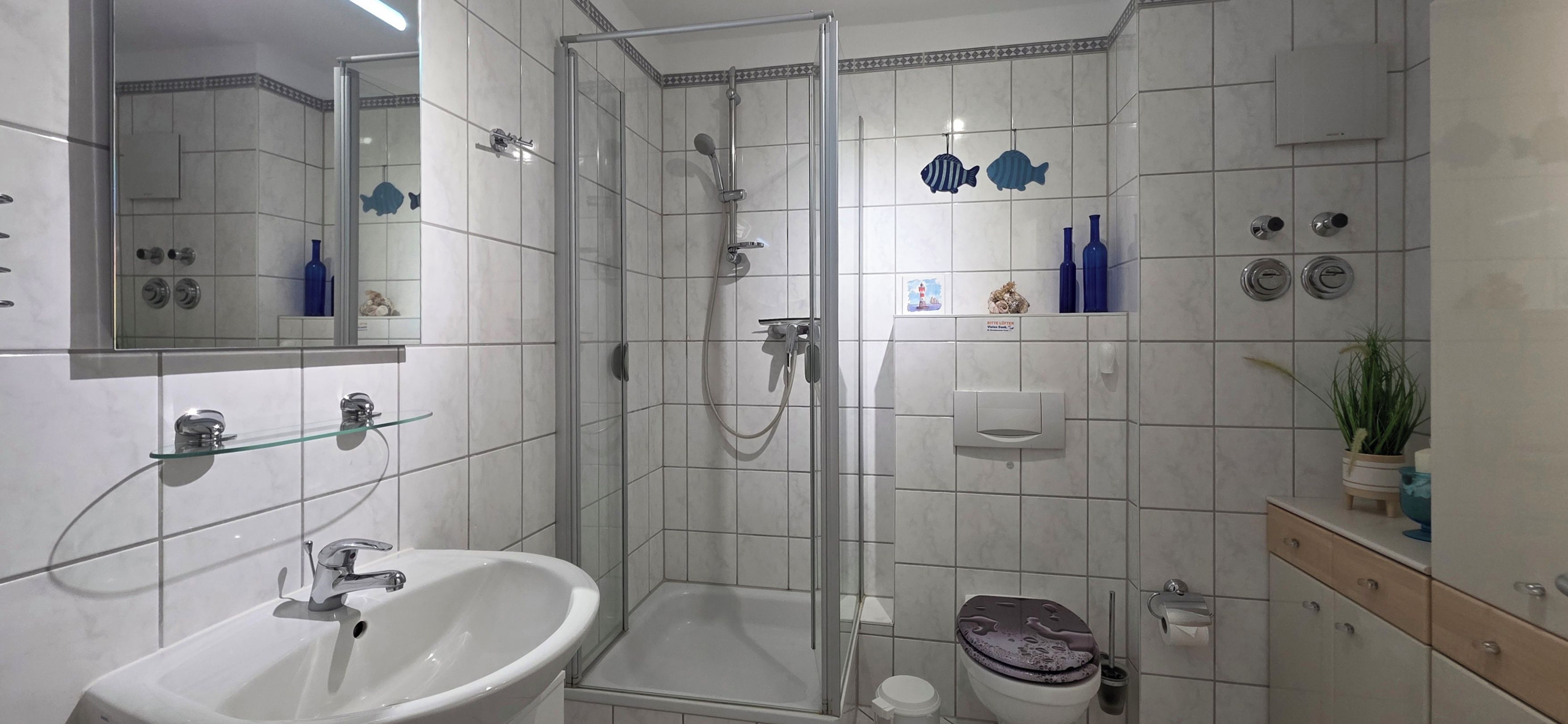Ein modernes Badezimmer mit einer gläsernen Dusche, einem weißen Waschbecken und einer Toilette.