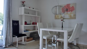 Un comedor con una mesa y sillas blancas, una estantería con diversos objetos y un cuadro en la pared.