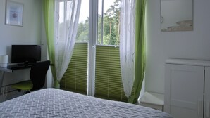 Un dormitorio con cama, escritorio, silla, televisión y ventana con cortinas.