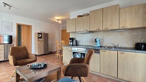 A modern kitchen with wooden cabinets, a stove, and a dishwasher. There is a dining area with two chairs and a table. - Strandnahe 2-zi-wohnung im Obergeschoss mit Zwei Balkonen (Graal-Müritz)