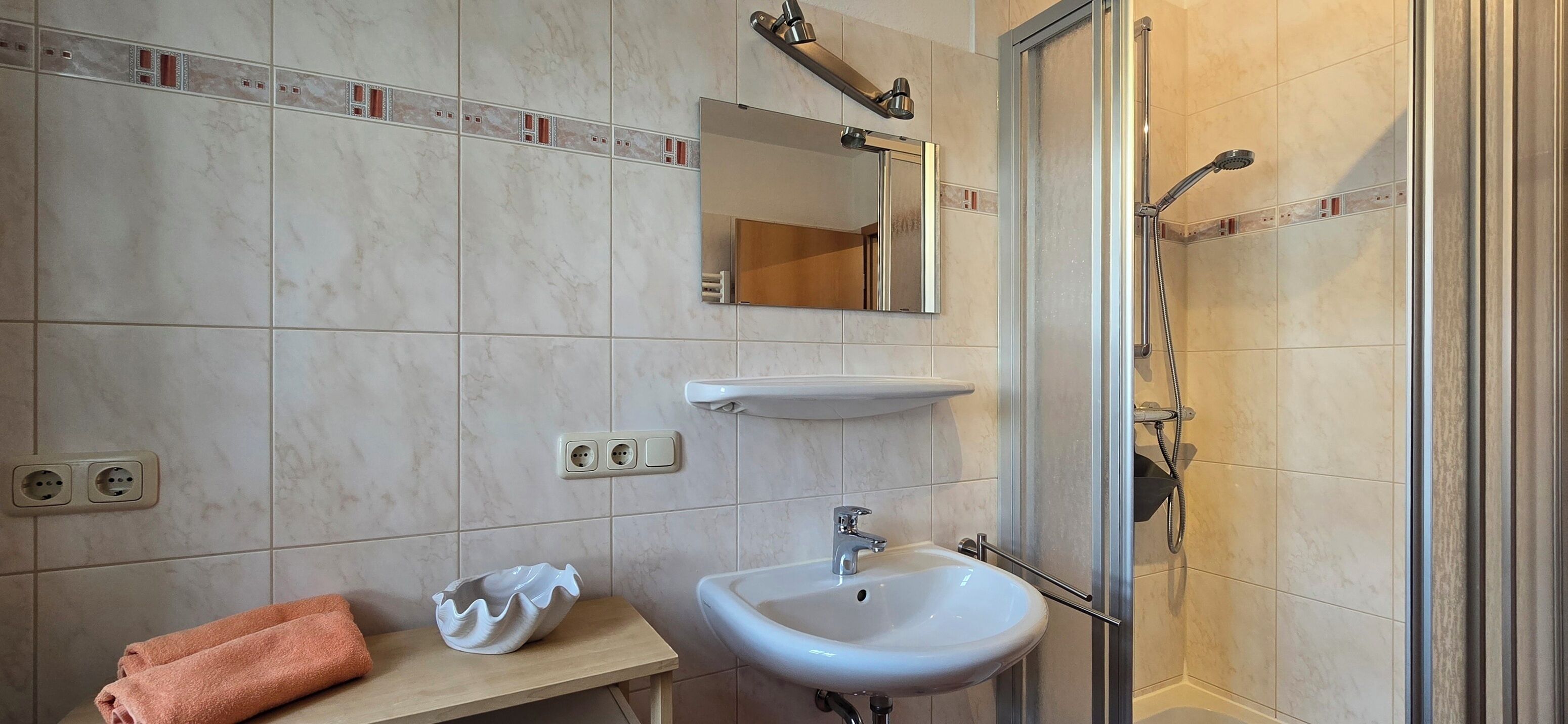 Een badkamer met een wastafel, spiegel en douche.
