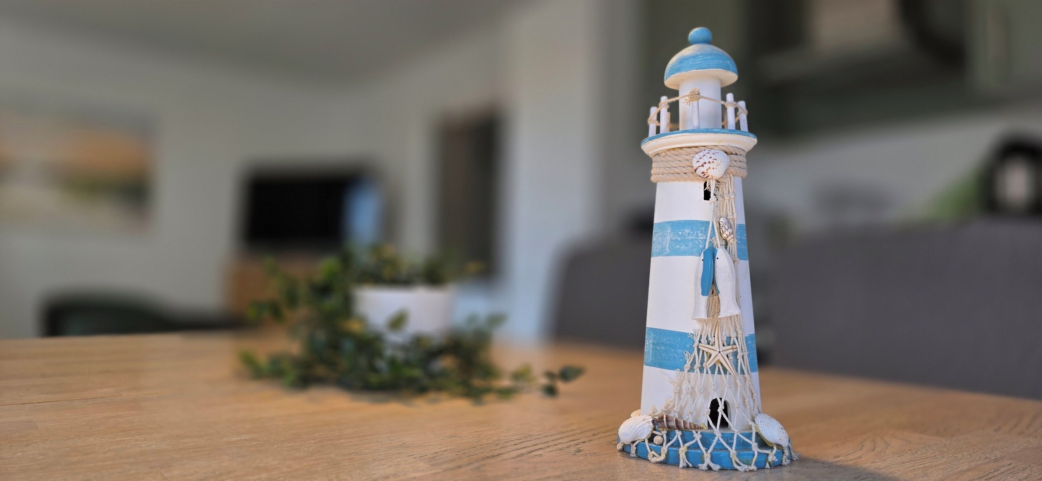 Un modellino di faro su un tavolo di legno, con uno sfondo interno sfocato.