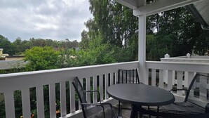 Un espacio al aire libre cubierto con una mesa y sillas, rodeado por una barandilla blanca, con vista a una zona residencial con árboles y casas.