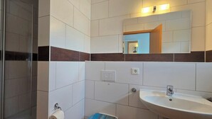 Un baño con ducha, lavamanos, espejo e inodoro.