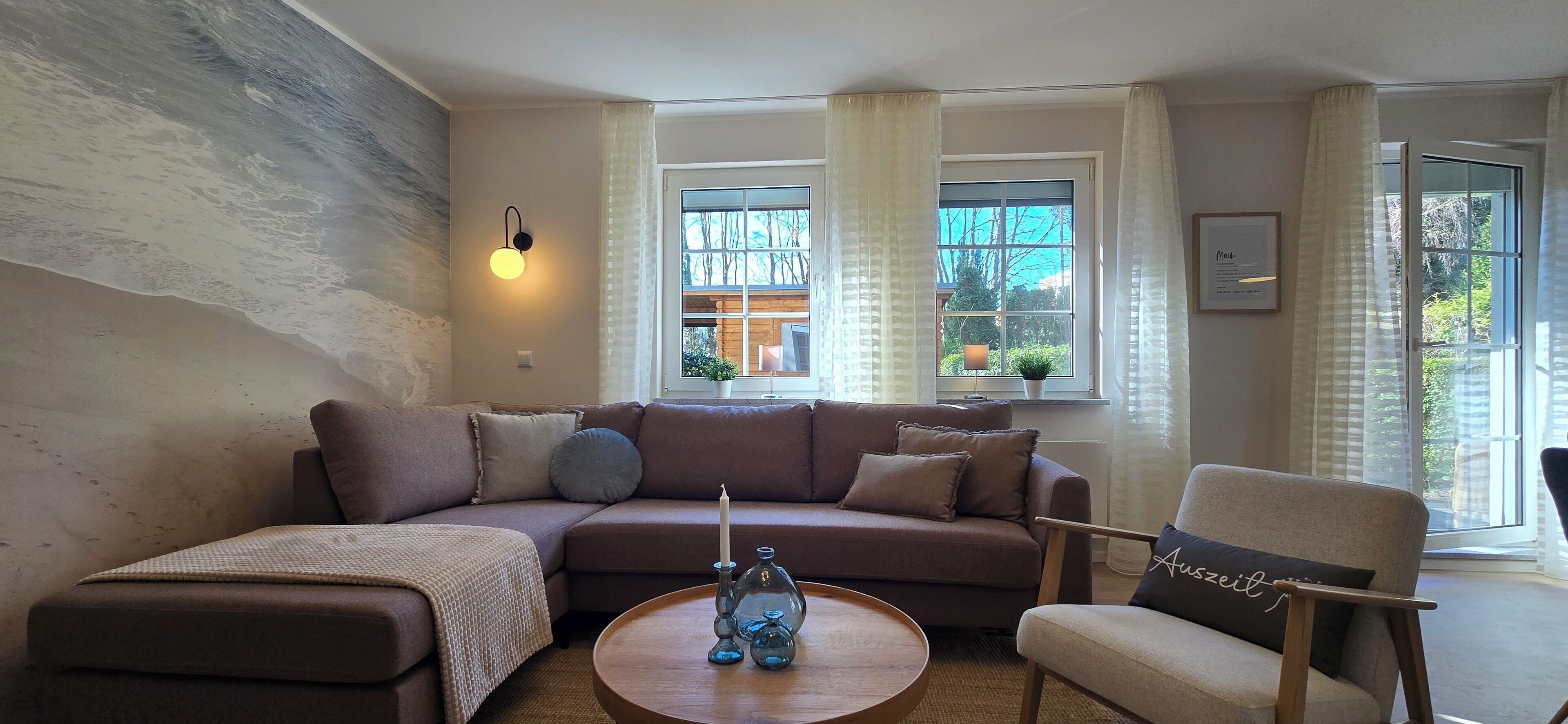 A cozy living room with a brown sofa, a round coffee table with decorative items, and a window with curtains.