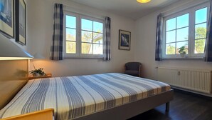 Ein Schlafzimmer mit einem Bett, zwei Vorhängen und einem Stuhl. Es gibt auch eine Heizung.