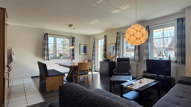Ein modernes Wohnzimmer mit Sofa, Couchtisch, Fernseher und Essbereich mit Tisch und Stühlen.