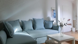 Ein modernes Wohnzimmer mit einem hellblauen Sofa, einem weißen Couchtisch und einem Korbstuhl.