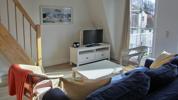 Ein modernes Wohnzimmer mit einem Fernseher auf einem weißen Schrank, einer Couch, einem Korbstuhl und einer Treppe.