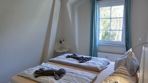Ein Schlafzimmer mit zwei Betten, einem kleinen Tisch mit einer Vase und einem Fenster mit Vorhängen.
