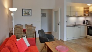Un espacio habitable compacto con kitchenette, una zona de comedor con mesa y sillas, y un sofá con cojines.