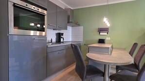 Une cuisine moderne avec des meubles gris, un four encastré, une machine à café et un coin repas comprenant une table ronde et quatre chaises.