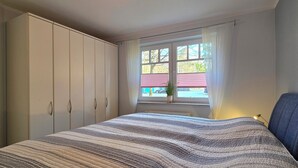 Une chambre à coucher avec un lit, une fenêtre avec des rideaux, une plante en pot et une armoire.