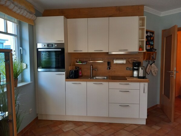 A compact kitchen with white cabinets, a built-in oven, and a sink. - Zentrale 2 Zimmer-fewo für 4 Pers., Terrasse mit Strandkorb (Graal-Müritz)