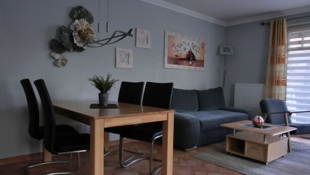 A modern living room with a dining table, chairs, a sofa, and a coffee table. - Zentrale 2 Zimmer-fewo für 4 Pers., Terrasse mit Strandkorb (Graal-Müritz)