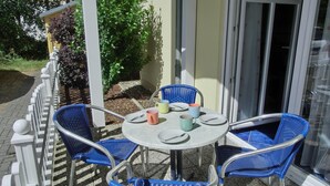 Un patio con una mesa redonda y cuatro sillas azules, rodeado por una valla blanca y follaje.