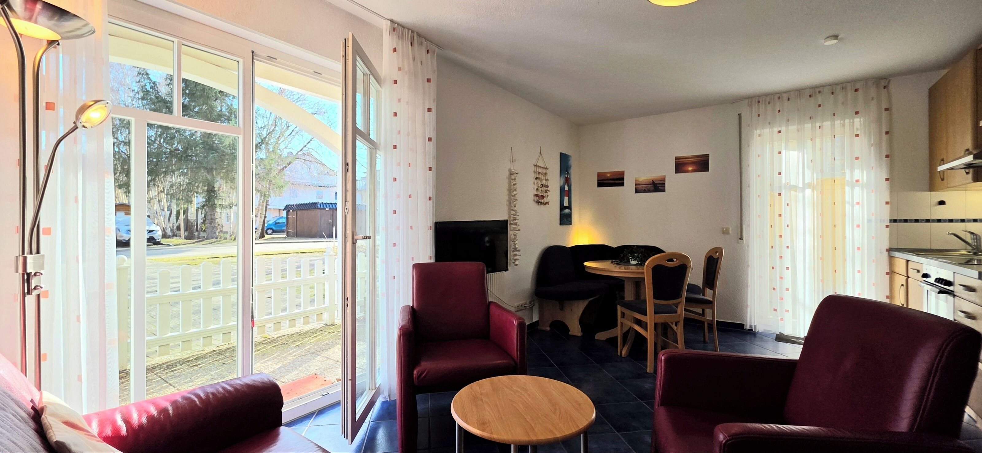 A room with a large sliding glass door leading to a balcony, a small round table, and two red armchairs.