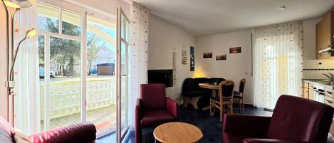 A room with a large sliding glass door leading to a balcony, a small round table, and two red armchairs.