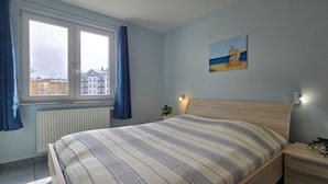 Une chambre à coucher avec un lit, une fenêtre avec des rideaux, une table de chevet avec une lampe et un tableau accroché au mur.