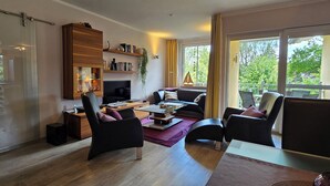 A modern living room with a sofa, chairs, a coffee table, and a TV. There are shelves with decorative items and a plant. - Luxuriöse 3-zi.-fewo für 4 Pers., Inklusive Bettwäsche, Handtücher und Wlan (Graal-Müritz)
