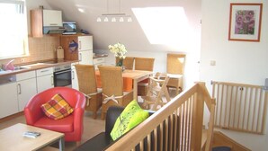 Una cocina compacta con electrodomésticos modernos, un comedor con mobiliario de mimbre y una escalera que sube a un dormitorio en el altillo.