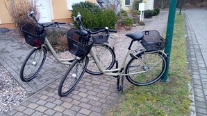 Dos bicicletas estacionadas en una zona pavimentada, con un edificio al fondo.