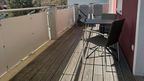 A covered outdoor deck with a table and chairs, a railing, and a view of trees and buildings.