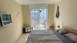 A bedroom with a bed, a suitcase, a TV, and a window with a view of buildings.