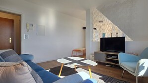 Ein modernes Wohnzimmer mit einer Couch, einem Couchtisch, einem Fernseher und einem Sessel.
