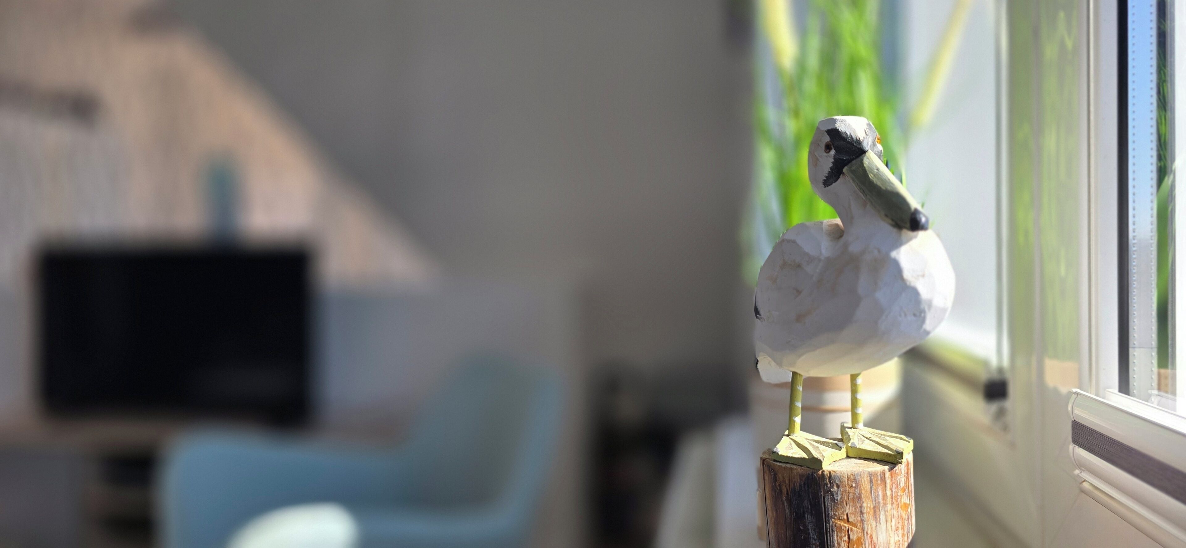 Une statuette d’oiseau posée sur un poteau en bois près d’une fenêtre.