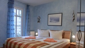 A bedroom with a bed, a nightstand, a lamp, a window with curtains, a wall-mounted picture, and a wall-mounted light fixture. - Strandnahe 3-zi-wohnung im Erdgeschoss mit Wlan (Graal-Müritz)