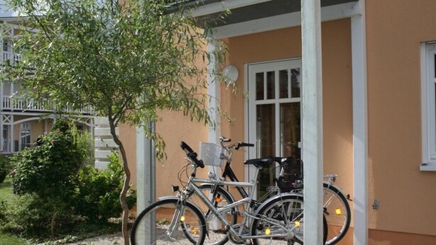 A bicycle parked under a covered area with a building in the background. - Strandnahe 3-zi-wohnung im Erdgeschoss mit Wlan (Graal-Müritz)
