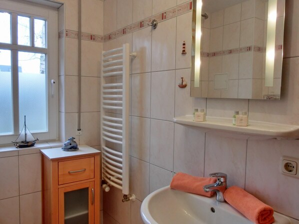 A bathroom with a white sink, a mirror, a towel, a window, and a radiator.