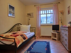 Une chambre à coucher comprenant un lit, une commode, un téléviseur, une fenêtre avec des rideaux et un radiateur.