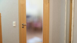 Una habitación con puerta de madera, una ventana pequeña y suelo de baldosas.