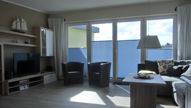 A modern living room with a flat-screen TV, two armchairs, a sofa, a coffee table, and a large window with a view of the sea. - 3-zimmer-fewo mit 2 SZ für 4 Pers.wlan (Graal-Müritz)