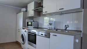 A compact kitchen with a washing machine, microwave, coffee maker, and built-in oven. - 3-zimmer-fewo mit 2 SZ für 4 Pers.wlan (Graal-Müritz)