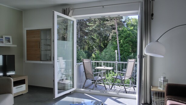 A modern living room with a glass door leading to a balcony, a flat-screen TV, a coffee table, and a sofa. - 3- Zi.-fewo mit 2 Schlafzimmern auf 2 Etagen für 4 Pers. mit Wlan (Graal-Müritz)
