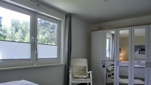 A bedroom with a bed, a chair, a wardrobe, and a window with blinds. - 3- Zi.-fewo mit 2 Schlafzimmern auf 2 Etagen für 4 Pers. mit Wlan (Graal-Müritz)