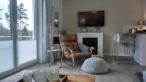 Ein modernes Wohnzimmer mit Ledersessel, Kamin, Wand-Fernseher und einer kleinen Küchenzeile mit Barhocker.