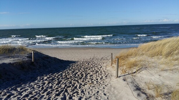 Ein Sandstrand mit einer Holzpromenade, die zum Meer führt.