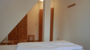 Un dormitorio con una cama, un armario de madera, un taburete y una puerta.