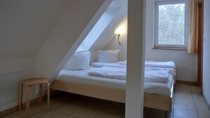 A small, single-bed room with a sloped ceiling, a window with curtains, and a bedside table. - 2-zimmer-ferienwohnung für 4 Personen im 1. Obergeschoss -mit Wlan (Neu Hirschburg)