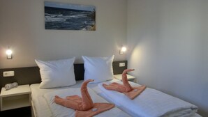 Ein Hotelzimmer mit zwei Betten, weißen Bettwäsche, einem Meeresbild an der Wand und Wandleuchten.