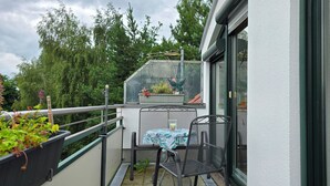 Varanda com mesa e cadeiras, um pequeno jardim e vista para árvores e um edifício.