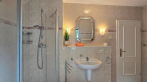Casa de banho com cabine de chuveiro envidraçada, lavatório suspenso e espelho sobre o lavatório.