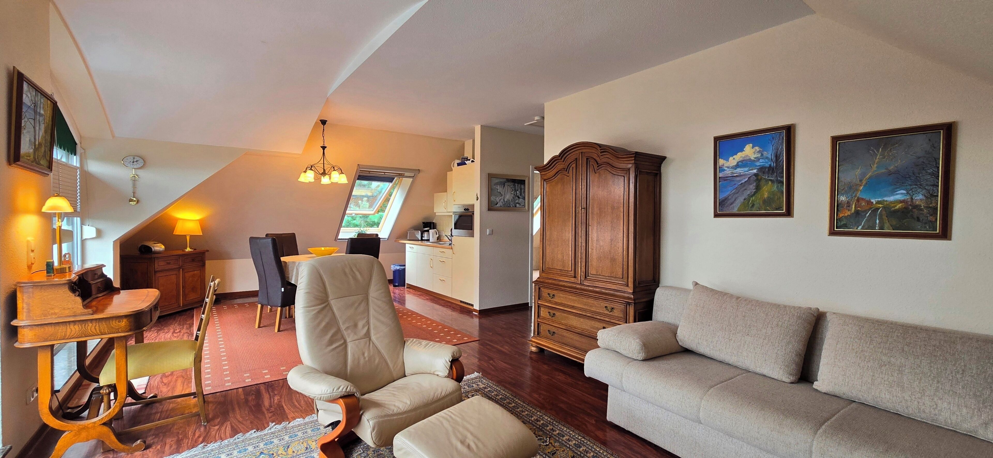 A spacious living room with a sofa, a dining area with a table and chairs, a wooden cabinet, and a painting on the wall.