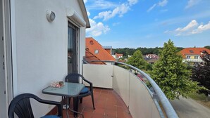 Un balcon avec une table et des chaises, une porte et une vue sur des maisons et des arbres.