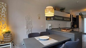 Moderni keittiö, jossa on ruokailutila, keskeinen keittiösaareke, riippuvalaisimet ja koristeellinen seinätaide.